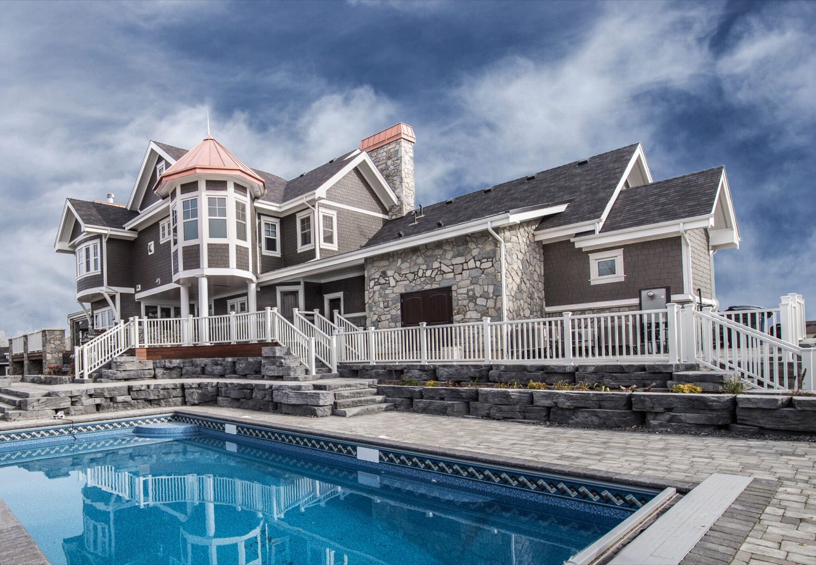 Estate home with stone masonry and a turret, seen across its rear pool deck
