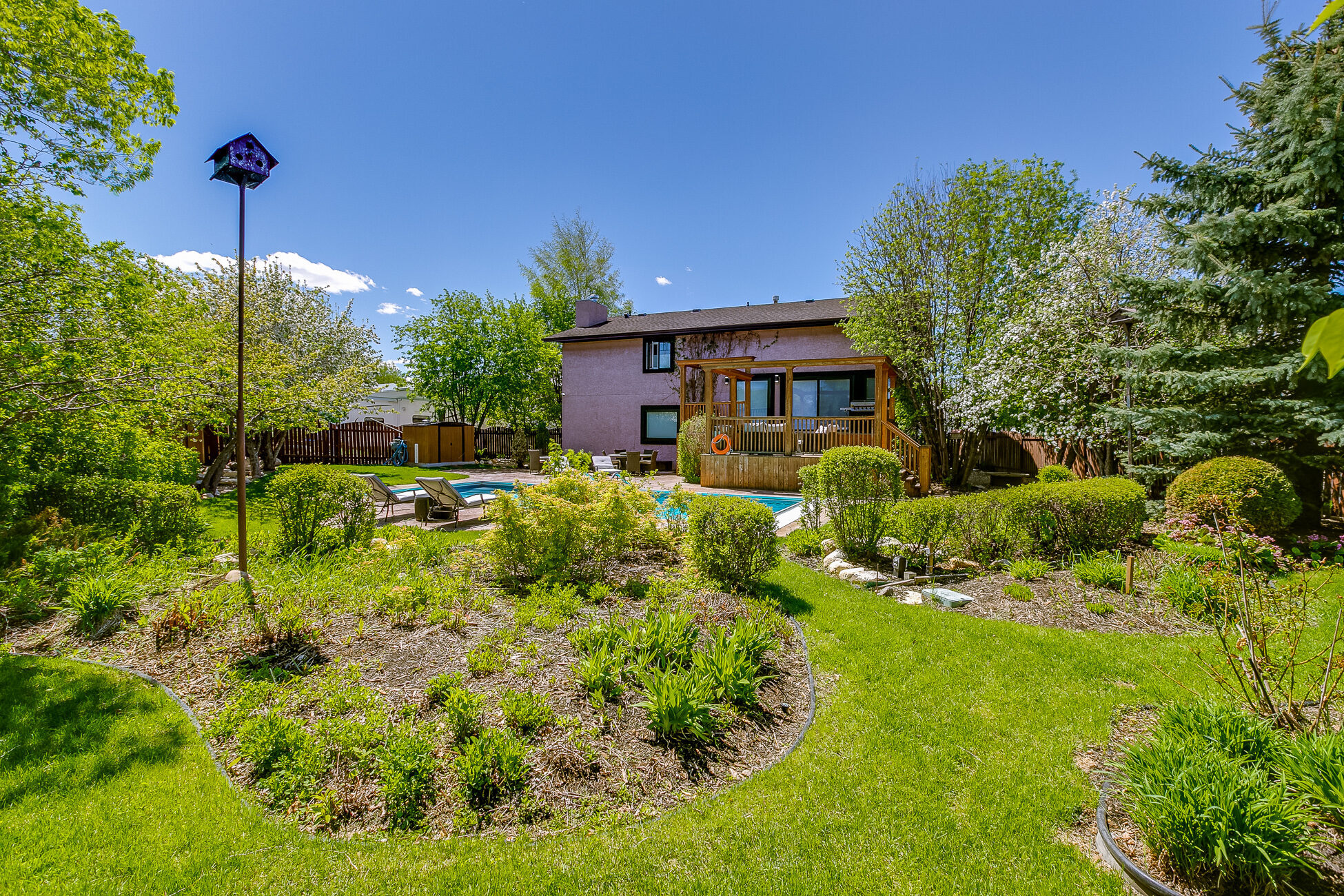 Landscaped backyard of 402 Coben in summer, with mature trees and garden beds