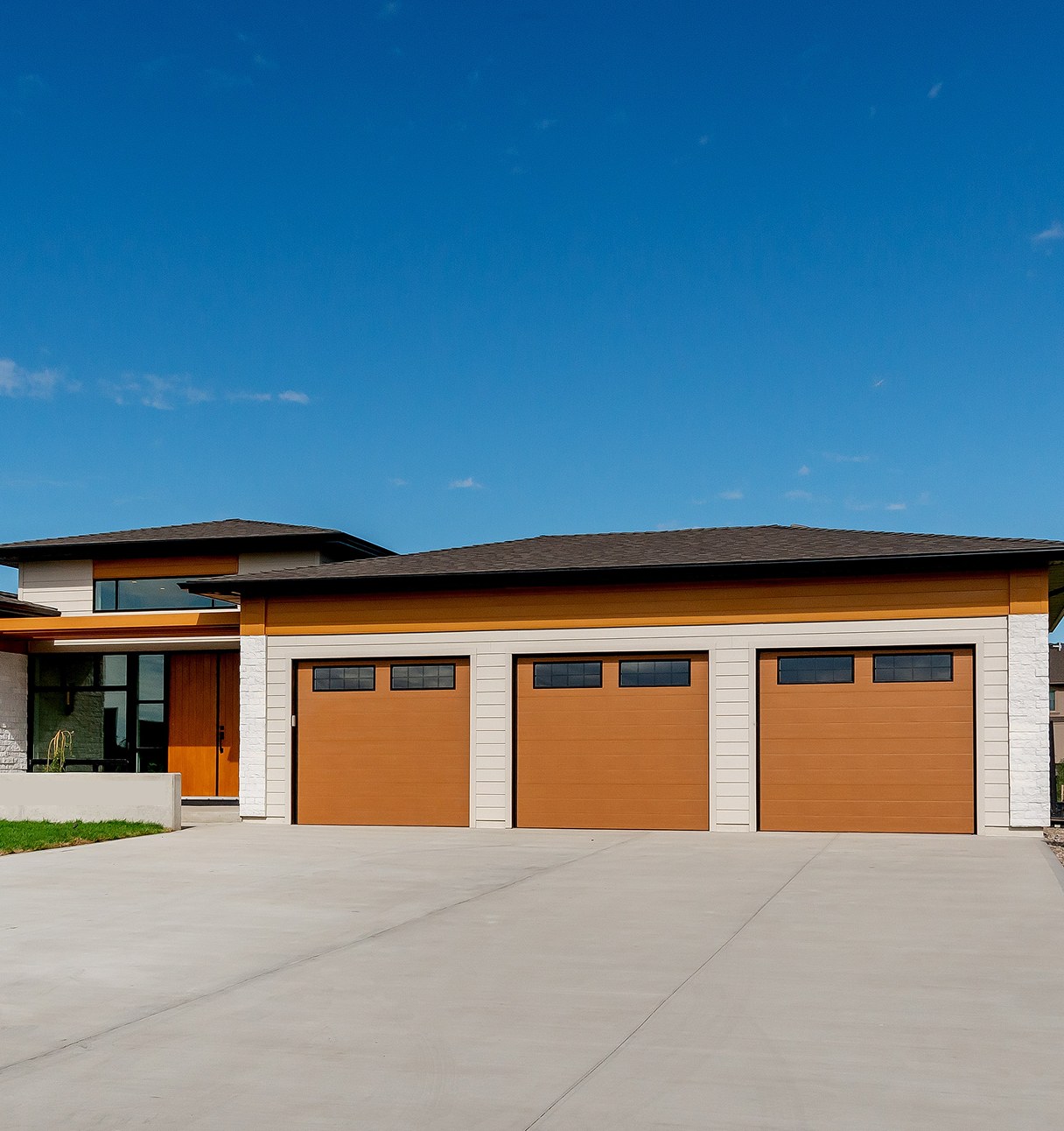 Contemporary Decora home with a triple garage of cedar-toned doors under a blue sky