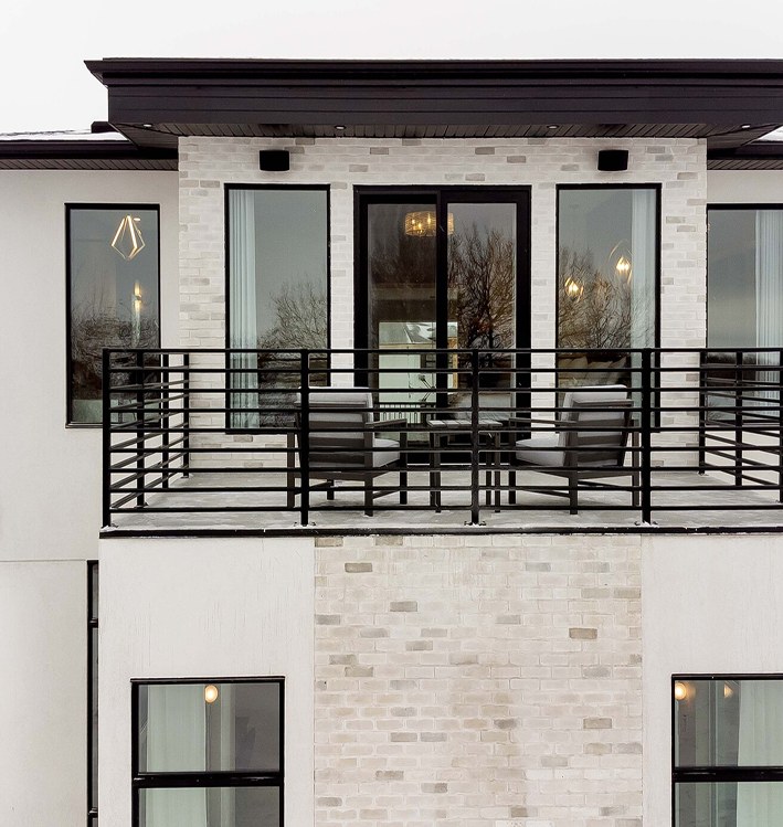Modern white façade with a black-railed balcony and stone at the base