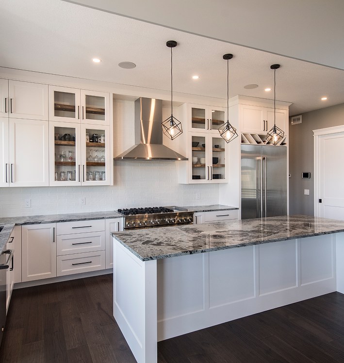 White kitchen with a marble island, pendant lights and a range hood