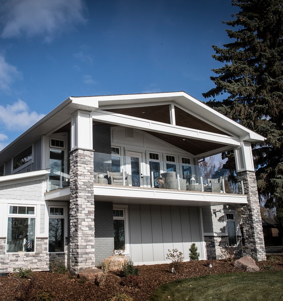 Two-storey walkout home with white siding and stone, its rear decks facing a lawn