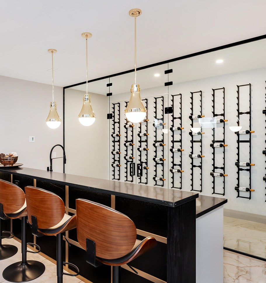 Kitchen island with leather stools in front of a lit glass wine wall