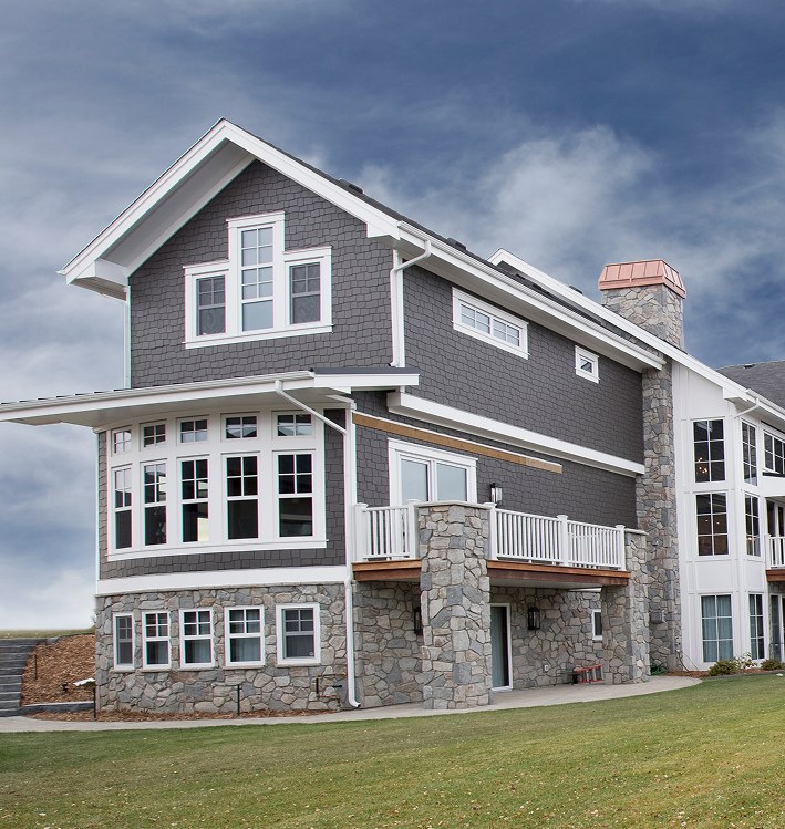 Three-storey grey home with stone at the base and white-trimmed windows