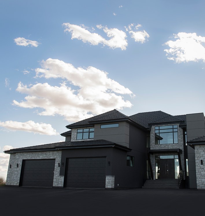 Large dark two-storey Decora home with a triple garage under a bright sky