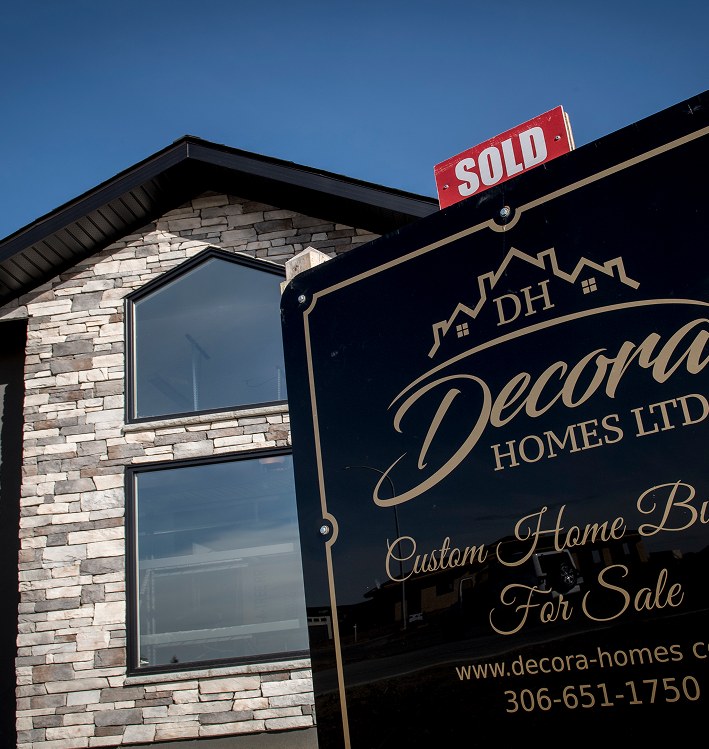 A Decora Homes “For Sale — Sold” sign in front of a stone-clad home